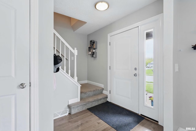 foyer entrance with baseboards, stairs, wood finished floors, and visible vents
