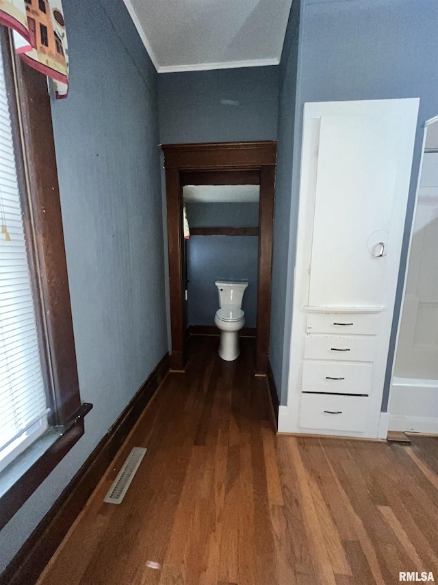 hallway featuring baseboards, ornamental molding, wood finished floors, and visible vents