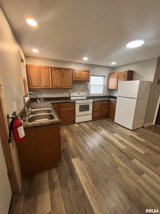 kitchen featuring dark countertops, a sink, white appliances, brown cabinetry, and dark wood-style floors