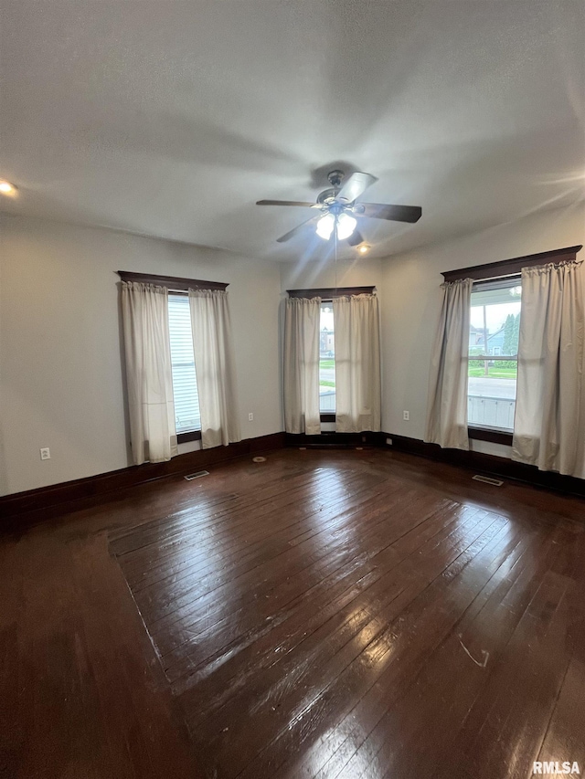 spare room with wood-type flooring, ceiling fan, visible vents, and baseboards