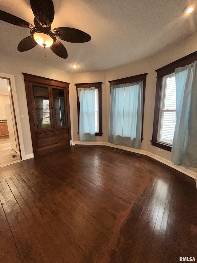 interior space with a healthy amount of sunlight, baseboards, a ceiling fan, and dark wood-type flooring