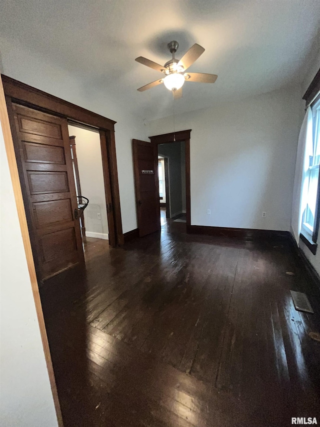 unfurnished room with baseboards, ceiling fan, and dark wood finished floors