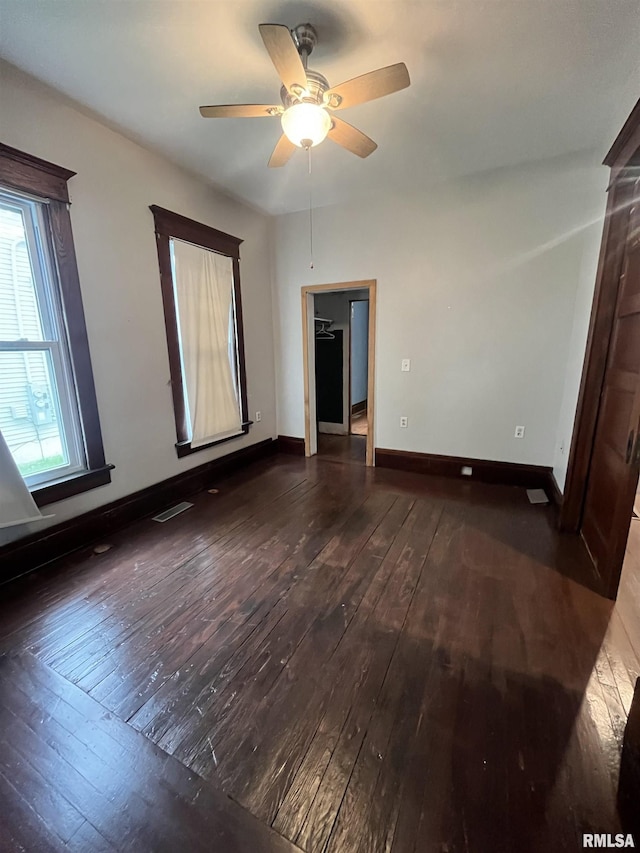 empty room with visible vents, a ceiling fan, dark wood-style flooring, and baseboards