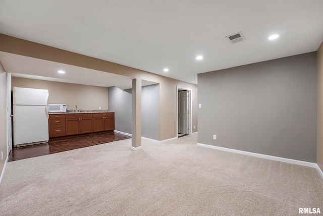 finished basement featuring dark colored carpet, freestanding refrigerator, recessed lighting, baseboards, and visible vents