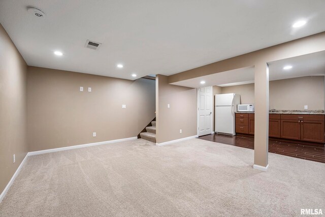 finished basement featuring baseboards, freestanding refrigerator, dark colored carpet, and visible vents