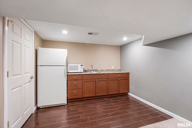 kitchen featuring white appliances, baseboards, wood finish floors, brown cabinets, and a sink