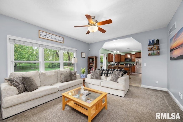 living room featuring visible vents, baseboards, light colored carpet, arched walkways, and ceiling fan with notable chandelier