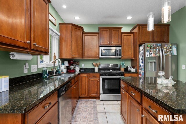 kitchen with hanging light fixtures, a sink, brown cabinetry, dark stone countertops, and stainless steel appliances