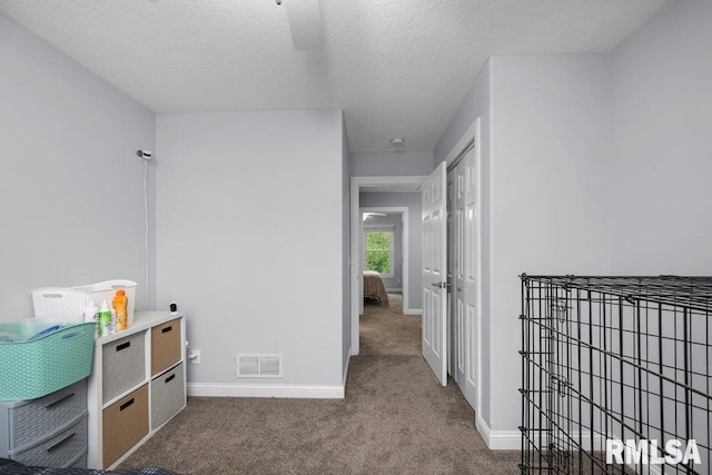 hall featuring a textured ceiling, baseboards, visible vents, and carpet