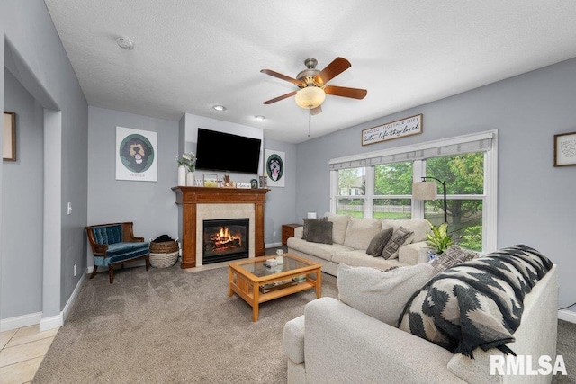 living room with ceiling fan, a tiled fireplace, baseboards, and light carpet