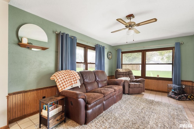 tiled living room featuring a ceiling fan, a wainscoted wall, and wooden walls