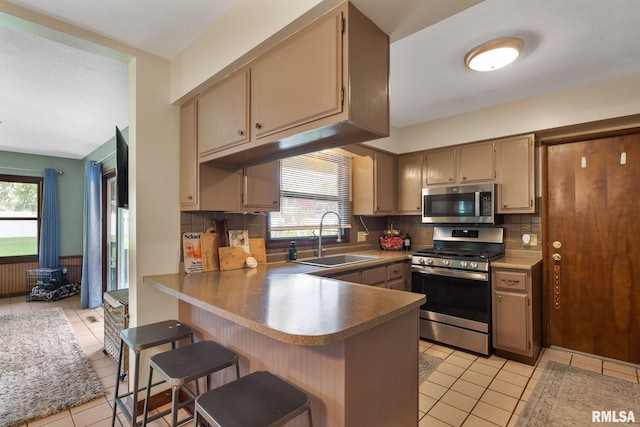 kitchen featuring decorative backsplash, a peninsula, a sink, light tile patterned floors, and stainless steel appliances
