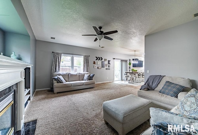 living area with carpet flooring, baseboards, a textured ceiling, a tile fireplace, and a ceiling fan