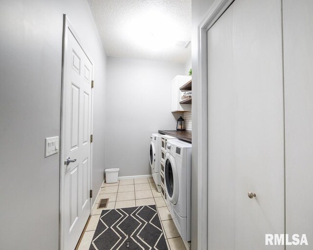 laundry room with a textured ceiling, visible vents, washing machine and clothes dryer, cabinet space, and light tile patterned floors