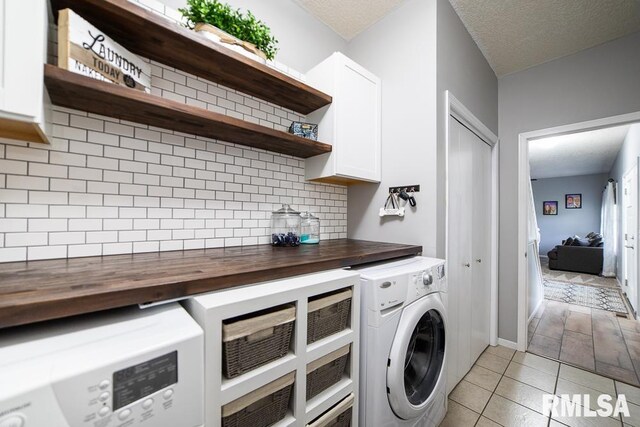 clothes washing area with light tile patterned floors, separate washer and dryer, a textured ceiling, and cabinet space