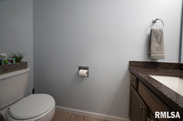 half bathroom with baseboards, vanity, toilet, and wood finished floors