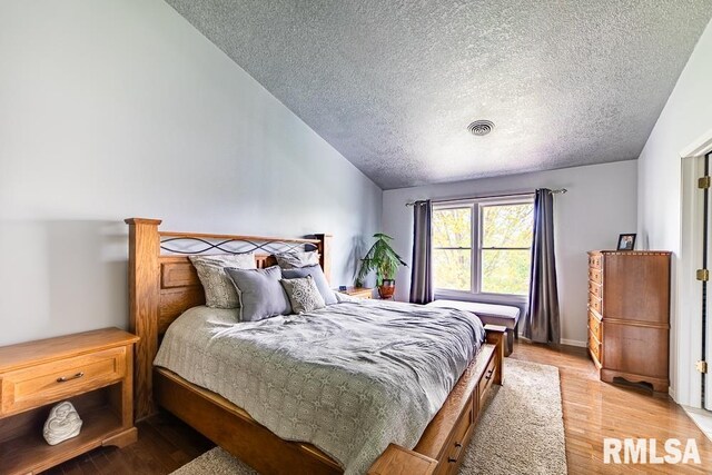 bedroom featuring a textured ceiling, visible vents, light wood-style flooring, and lofted ceiling