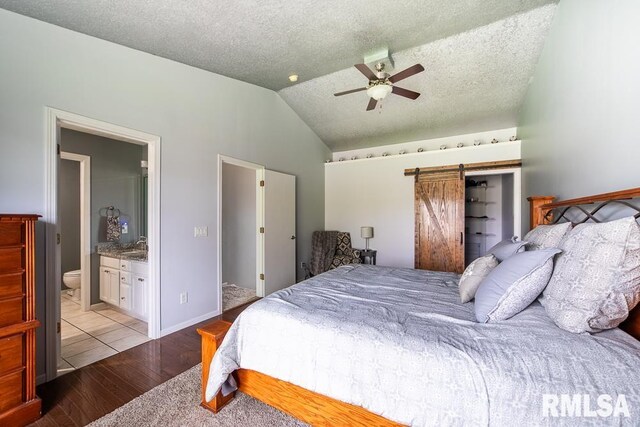 bedroom with a barn door, connected bathroom, a textured ceiling, light wood finished floors, and vaulted ceiling