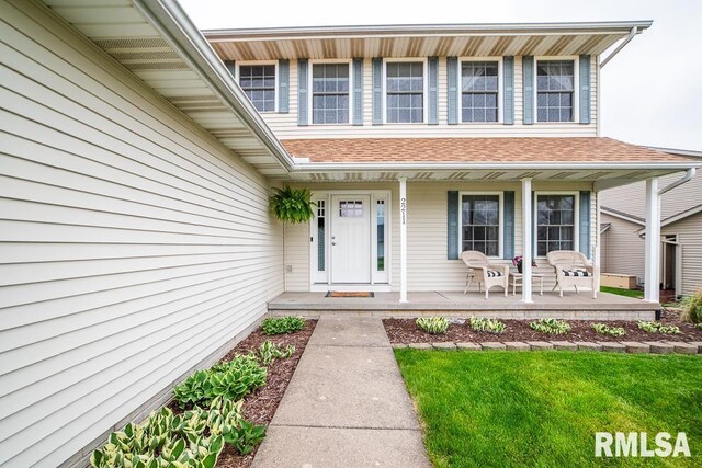 doorway to property featuring a lawn, a shingled roof, and a porch