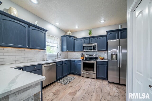 kitchen featuring a textured ceiling, blue cabinets, a sink, light wood finished floors, and stainless steel appliances