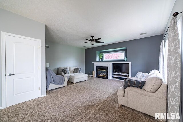 carpeted living room featuring a glass covered fireplace, ceiling fan, and visible vents