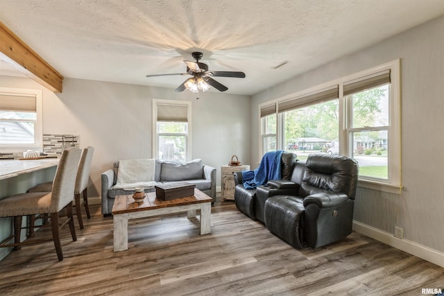 living area featuring baseboards, a ceiling fan, a textured ceiling, and wood finished floors
