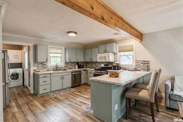 kitchen featuring plenty of natural light, washer / clothes dryer, appliances with stainless steel finishes, and a peninsula