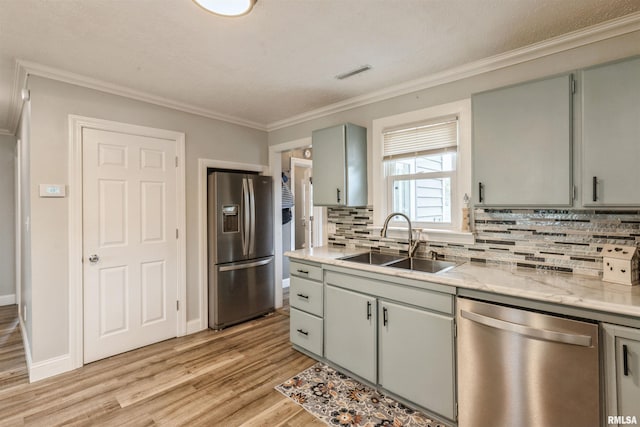 kitchen with backsplash, light wood-type flooring, a sink, ornamental molding, and stainless steel appliances