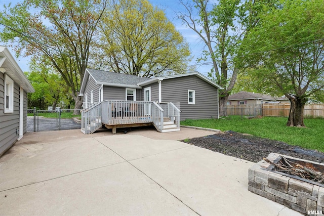 back of property featuring roof with shingles, a wooden deck, fence, an outdoor fire pit, and a patio