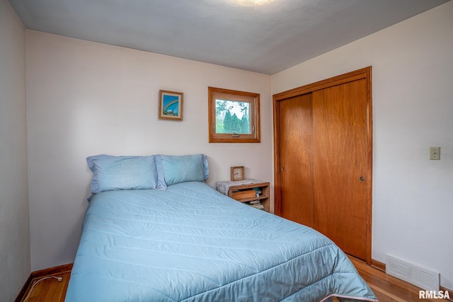 bedroom with baseboards, visible vents, wood finished floors, and a closet