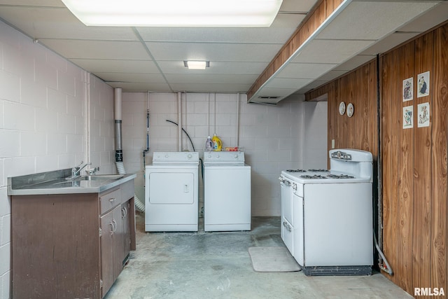 washroom with concrete block wall, wood walls, independent washer and dryer, and a sink