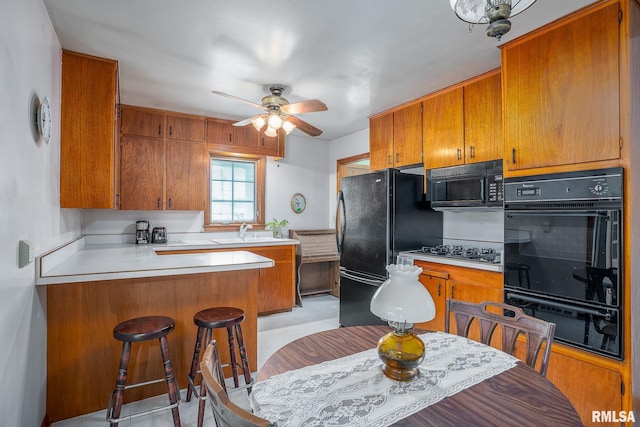 kitchen with a sink, a peninsula, brown cabinets, a ceiling fan, and black appliances