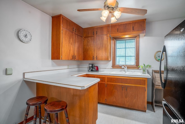 kitchen with a sink, light countertops, brown cabinetry, freestanding refrigerator, and a peninsula