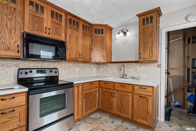 kitchen with brown cabinetry, black microwave, light countertops, stainless steel electric range, and a sink