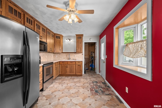 kitchen with brown cabinets, appliances with stainless steel finishes, light countertops, a ceiling fan, and decorative backsplash
