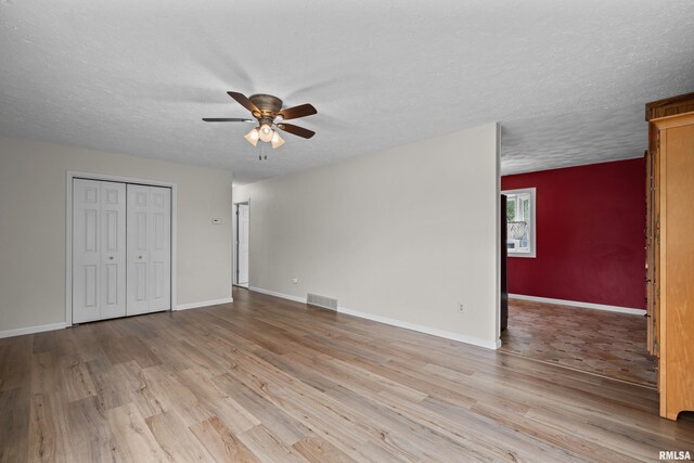 unfurnished bedroom featuring a textured ceiling, baseboards, light wood-type flooring, visible vents, and a closet