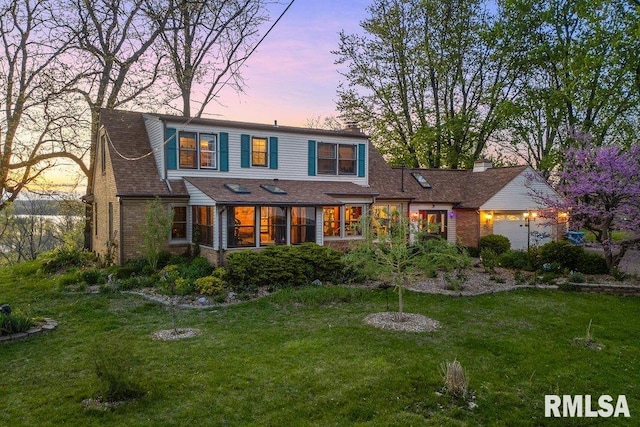 view of front of home with a sunroom, a chimney, a yard, and brick siding