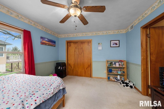 carpeted bedroom with visible vents, a ceiling fan, a wainscoted wall, and a closet