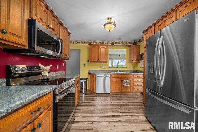 kitchen featuring brown cabinets, stainless steel appliances, a sink, and light wood finished floors