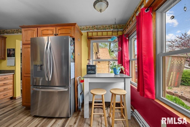 kitchen with stainless steel fridge, dark countertops, baseboard heating, and light wood-style flooring
