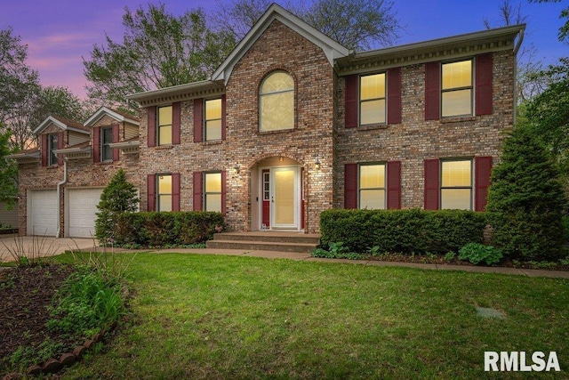 colonial house featuring a lawn, concrete driveway, a garage, and brick siding