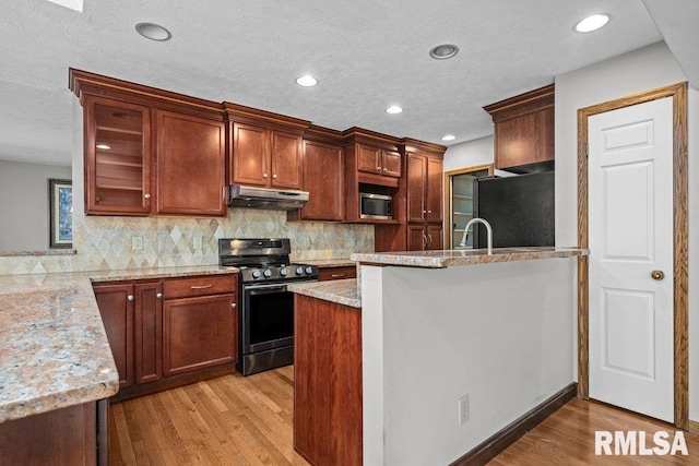 kitchen featuring light wood-style flooring, under cabinet range hood, light stone countertops, and stainless steel appliances