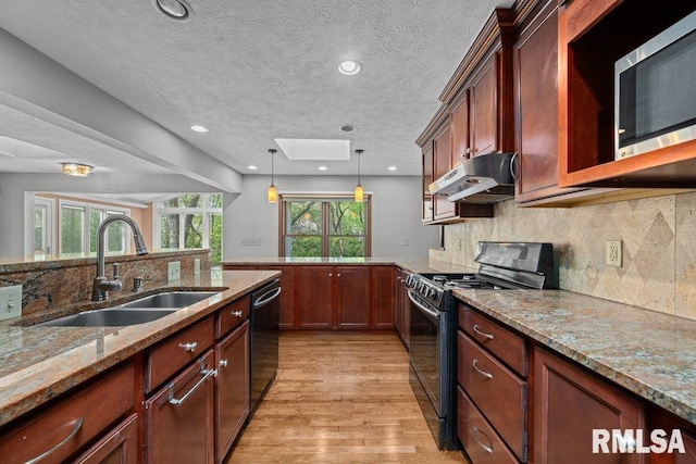 kitchen with a peninsula, under cabinet range hood, a sink, light wood finished floors, and black appliances