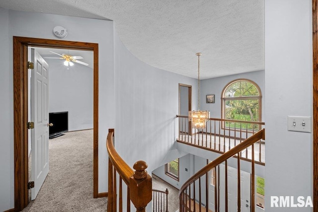 hallway with a textured ceiling, carpet, a notable chandelier, and an upstairs landing