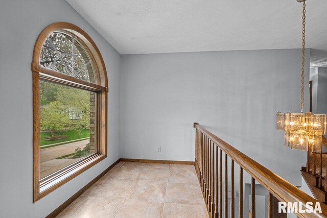 corridor featuring baseboards, light tile patterned flooring, a chandelier, and an upstairs landing