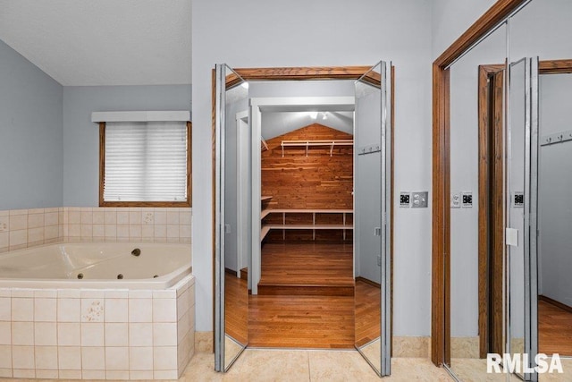 full bath with a whirlpool tub, a spacious closet, and vaulted ceiling