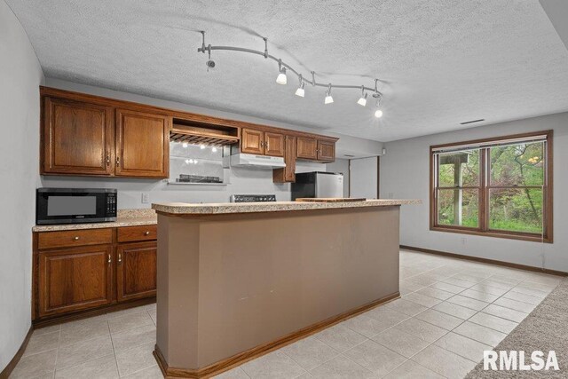 kitchen with a center island, brown cabinets, light tile patterned floors, freestanding refrigerator, and under cabinet range hood