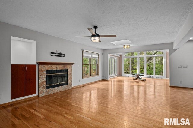 unfurnished living room featuring a tiled fireplace, baseboards, ceiling fan, and wood finished floors