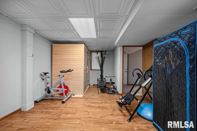 exercise room featuring light wood-style floors, baseboards, and an ornate ceiling