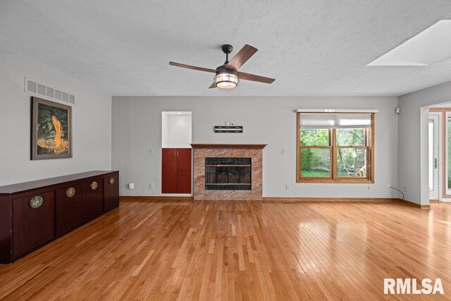 unfurnished living room featuring ceiling fan, a textured ceiling, visible vents, a fireplace, and light wood-type flooring